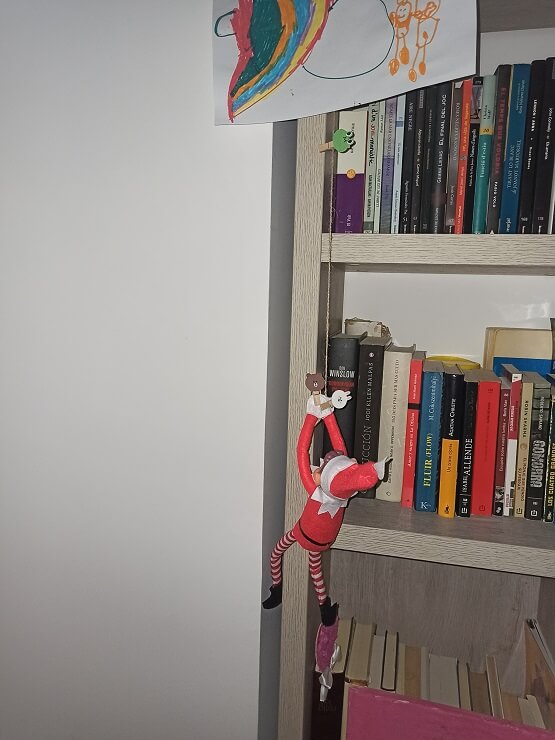 El elfo de Navidad escalando una estantería de libros.