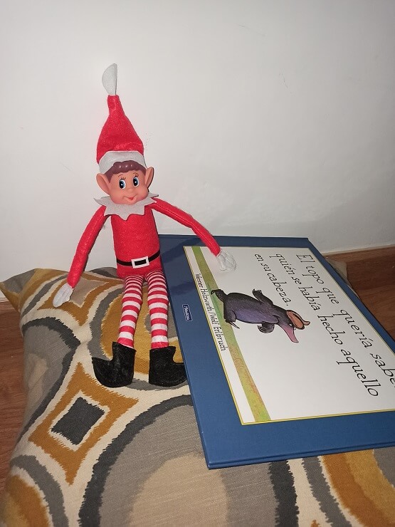 El elfo de Navidad con el libro "El topo que quería saber quién se había hecho aquello sobre su cabeza".